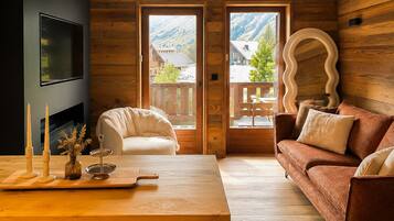 A cozy room with a wooden floor, a sofa, a chair, a table with candles, and a TV.