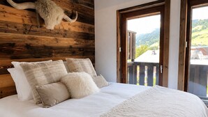 A bedroom with a wooden headboard, a bed with white bedding, and a view of a mountain landscape through a door. - Lutins Megève Village Sports Arena (Megève)