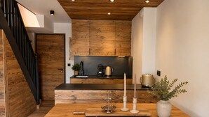 A modern kitchen with wooden cabinets, a black countertop, and a wooden dining table with candles and a vase. - Lutins Megève Village Sports Arena (Megève)