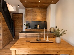 Eine moderne Küche mit Holzausbau, einer schwarzen Arbeitsplatte und einem Esstisch aus Holz mit Kerzen und einer Vase.
