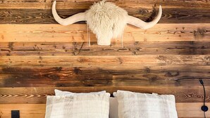 A bed with white bedding and fluffy pillows, a wooden headboard, and a large horn decoration. - Lutins Megève Village Sports Arena (Megève)