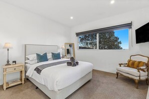 A bedroom with a bed, bedside tables, a chair, a window, and a television. - Ocean Views - just metres from the beach! (Ocean Grove)