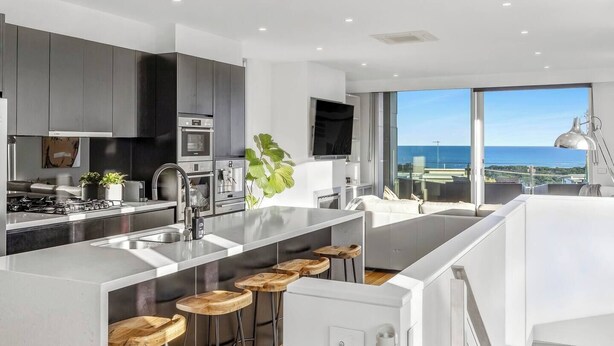 A modern kitchen with a large island, bar stools, and a view of the ocean. - Ocean Views - just metres from the beach! (Ocean Grove)
