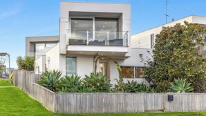 A modern two-story house with a balcony, a wooden fence, and various plants. - Ocean Views - just metres from the beach! (Ocean Grove)