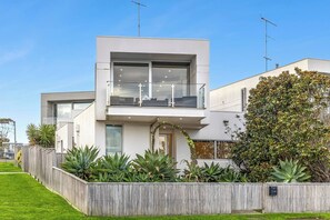 A modern two-story house with a balcony, a wooden fence, and various plants. - Ocean Views - just metres from the beach! (Ocean Grove)