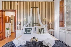 Ein Schlafzimmer mit einem Himmelbett, zwei Nachttischlampen, einem Fenster mit Vorhängen und einer Heizung.