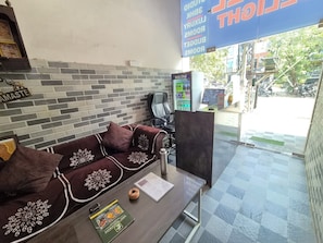 Uma área de recepção com sofá, mesa de centro, menu e um painel informativo listando comodidades como quarto, sala de estar e piscina.