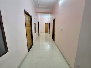 Um corredor com portas em ambos os lados, piso ladrilhado e teto com iluminação embutida.