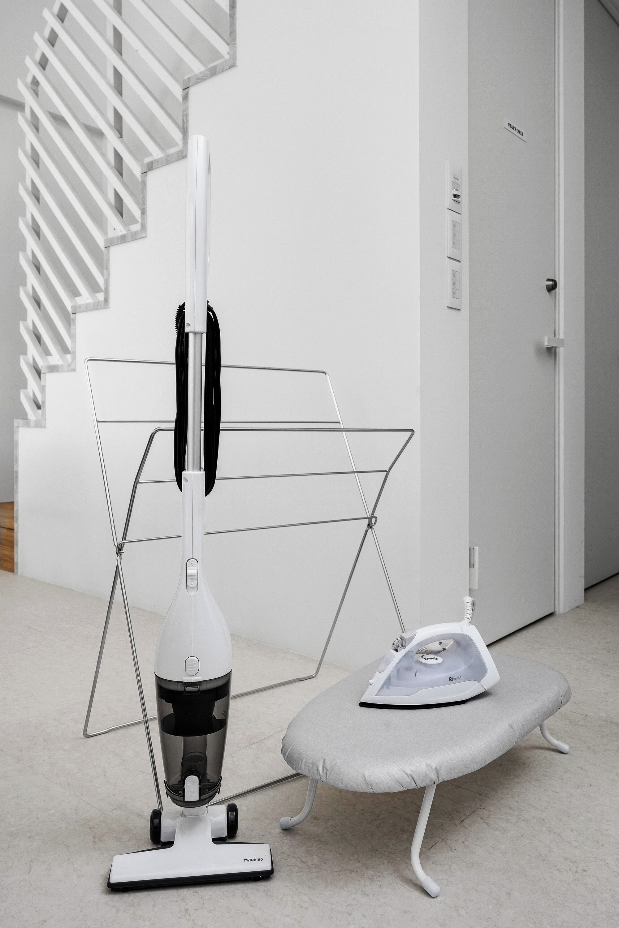 Una habitación moderna con aspiradora, tabla de planchar y una escalera.