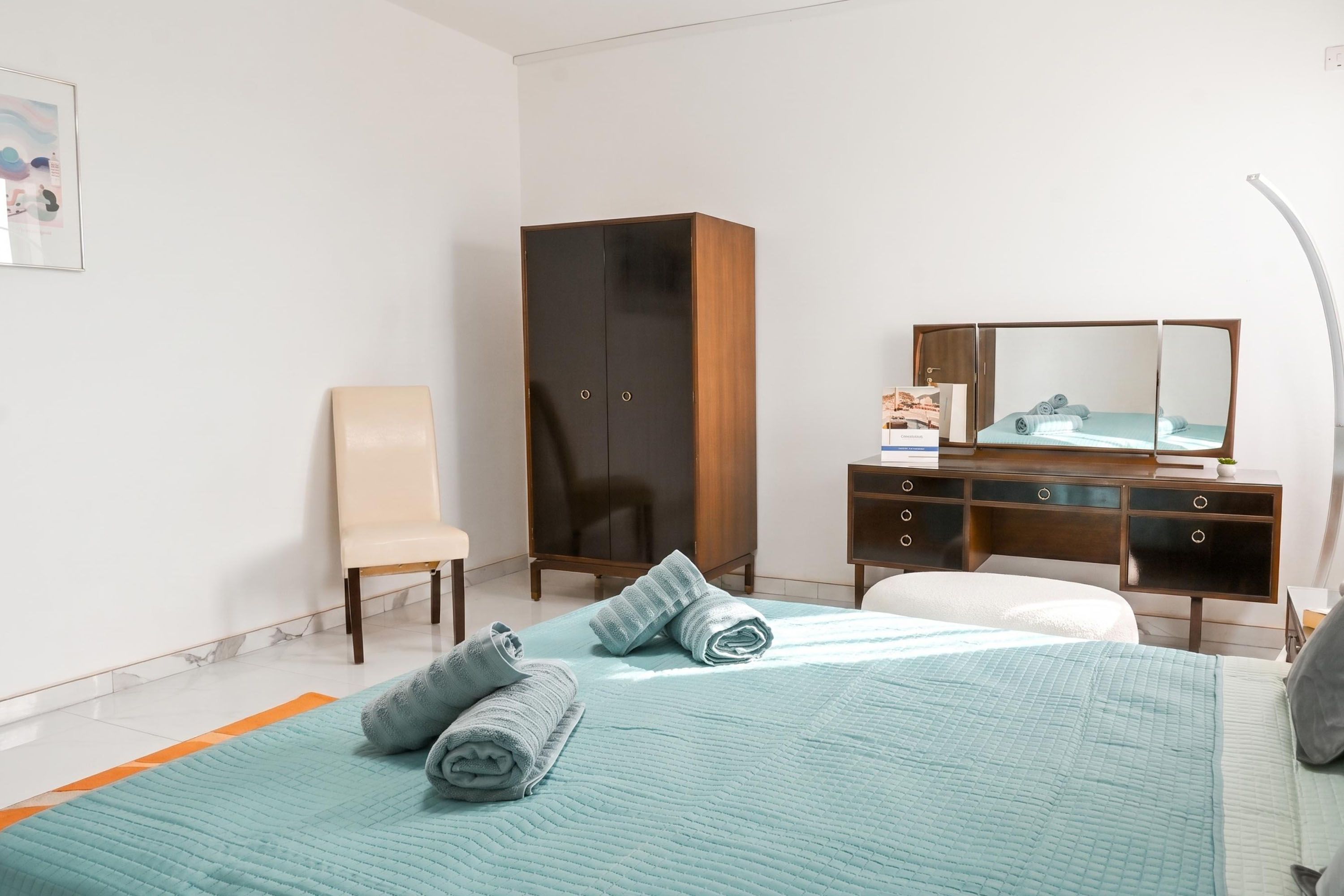 A hotel room with a bed, a chair, a wardrobe, a desk, and a mirror.