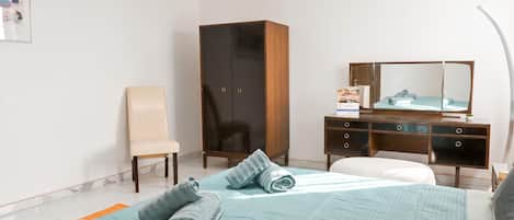 Habitación de hotel con cama, una silla, armario, escritorio y espejo.