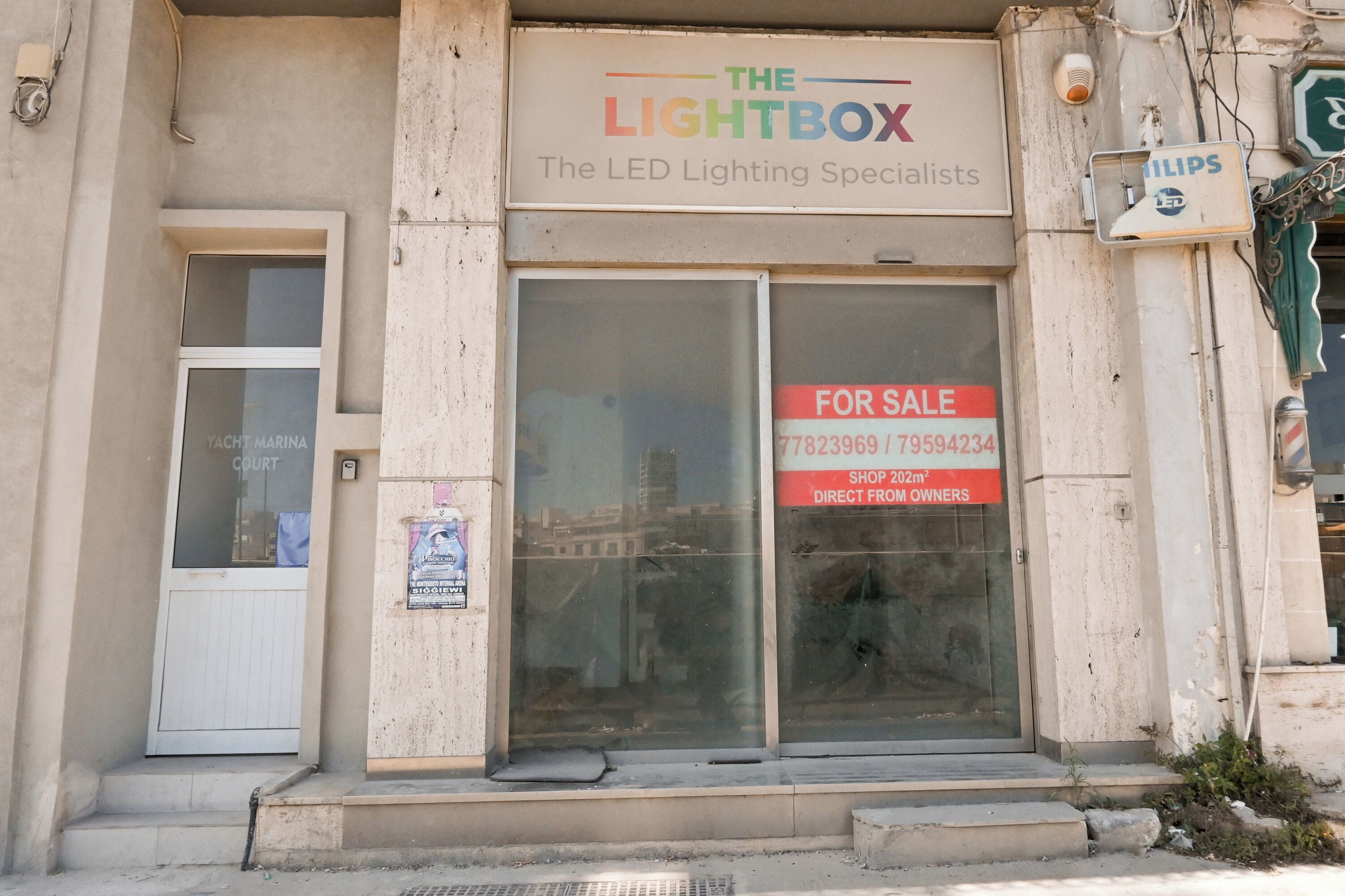 Ein Gebäude mit einem Schild für 'The Lightbox – The LED Lighting Specialists' und einem 'Zu verkaufen'-Schild.