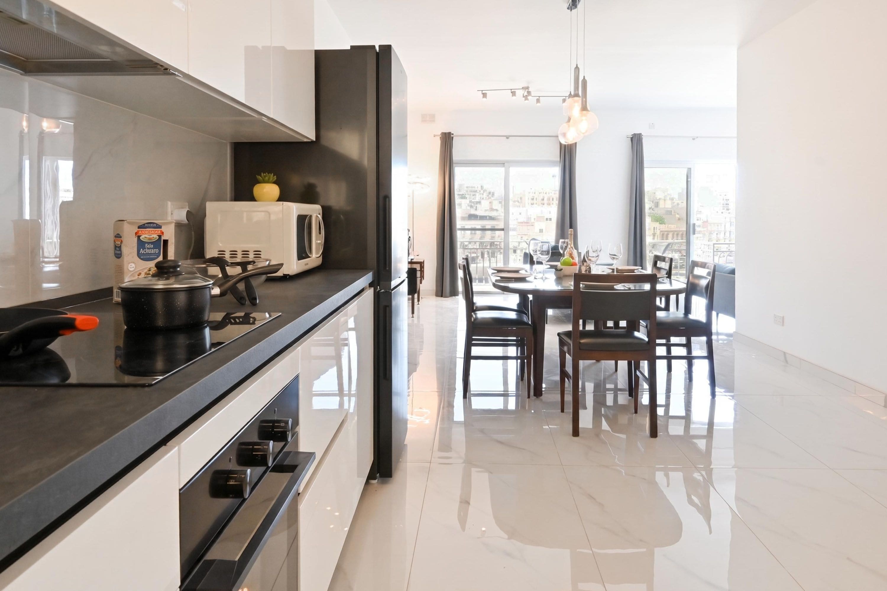 A modern kitchen with a black countertop, white appliances, and a dining area with a view.
