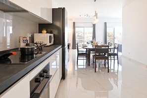 A modern kitchen with a black countertop, white appliances, and a dining area with a view. - Yacht Marina View - Modern 3 Bdrs Apart M (Msida)
