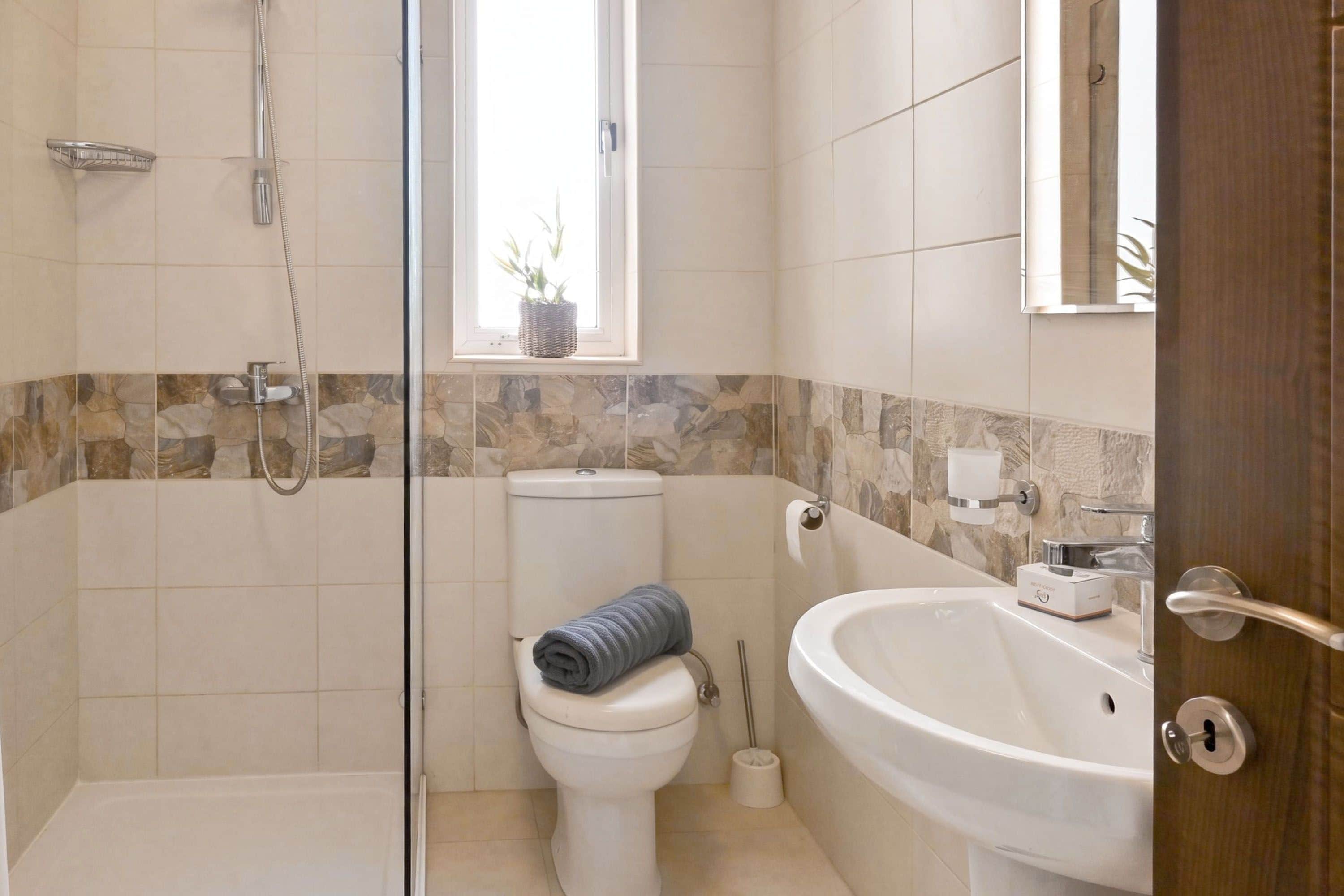 Ein Badezimmer mit Duschkabine aus Glas, Toilette, Waschbecken und einem Fenster mit Pflanze.