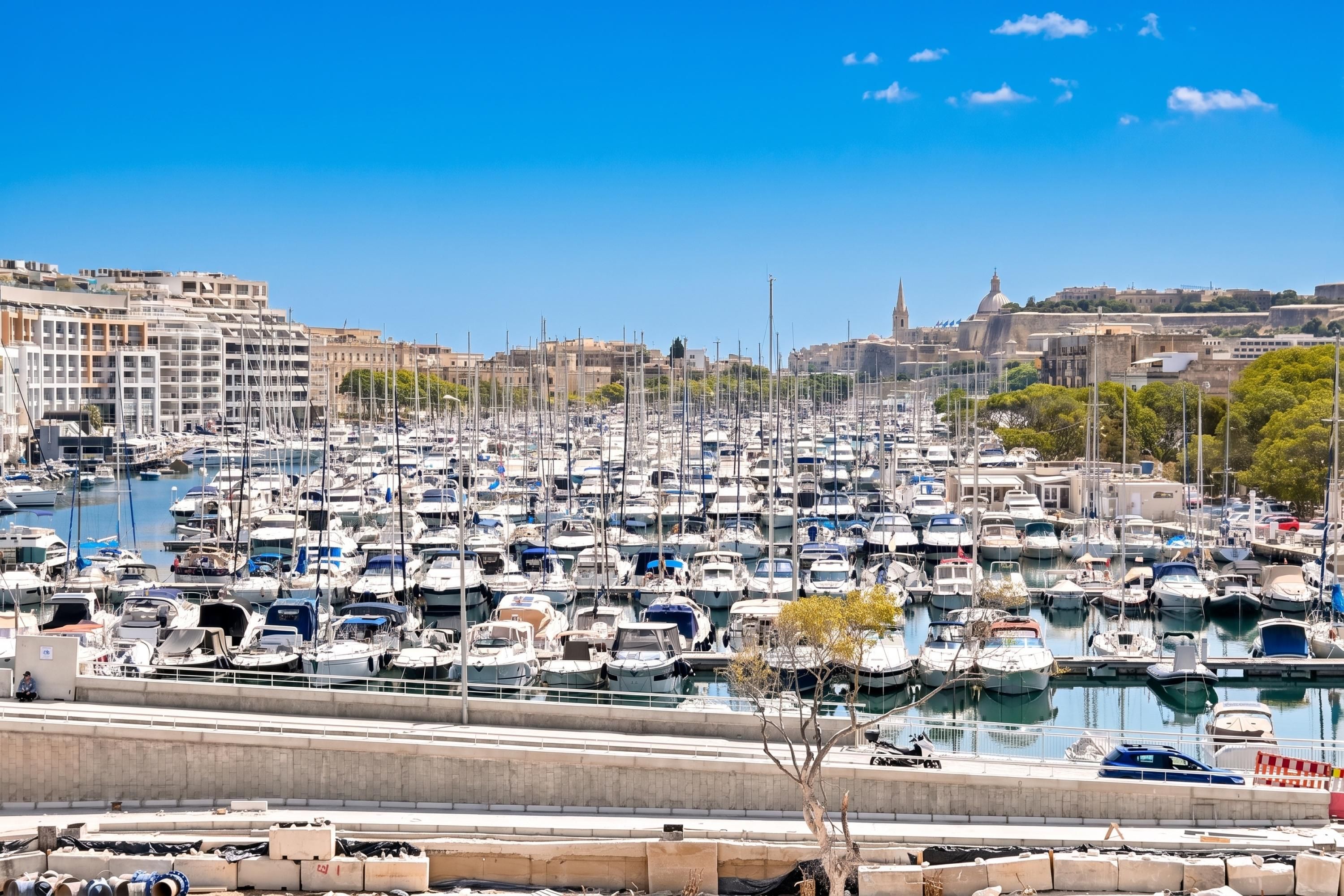 A marina filled with numerous boats docked in a harbor with buildings in the background.