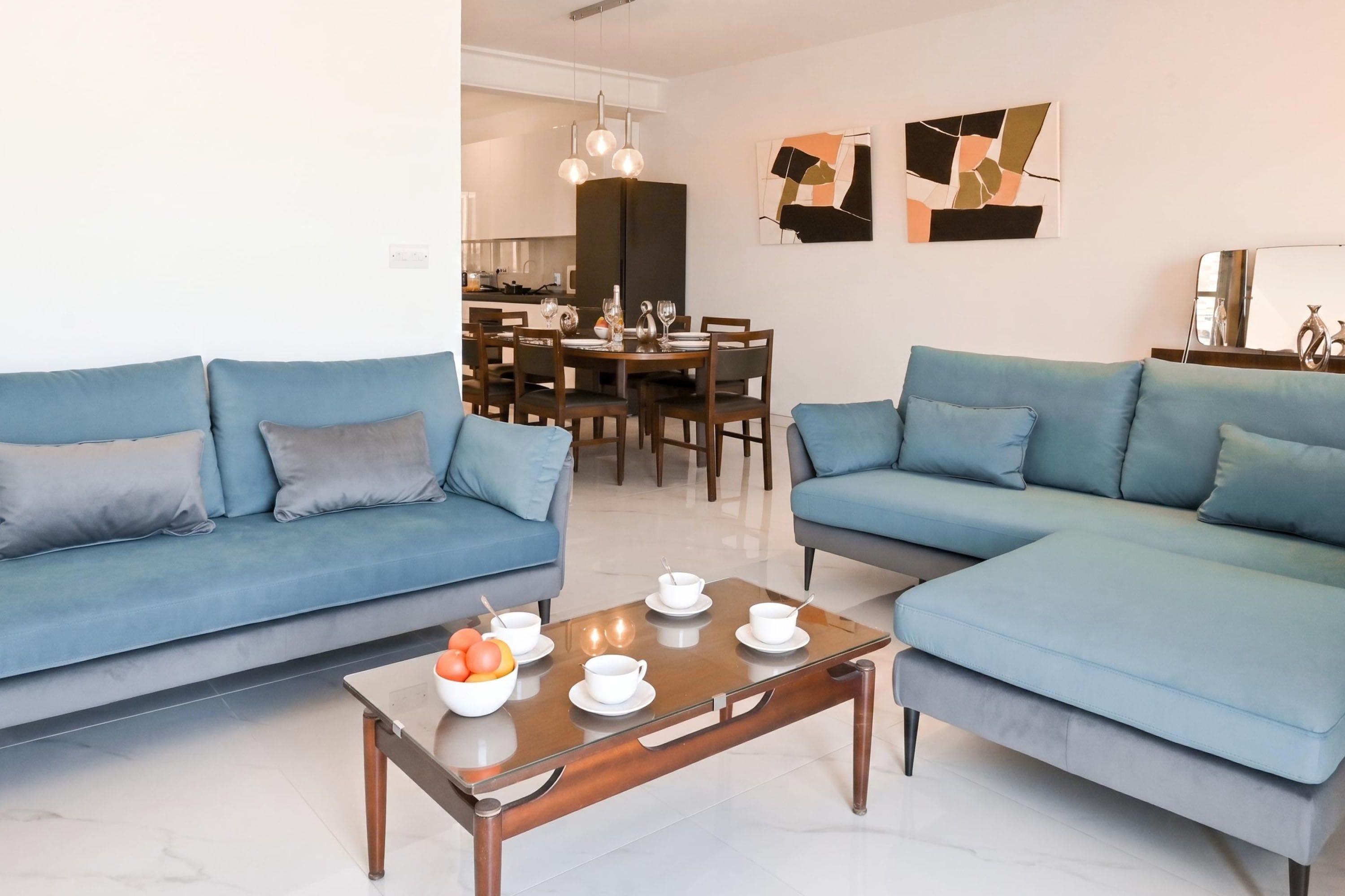 Ein modernes Wohnzimmer mit zwei Sofas, einem Couchtisch mit Schalen und Früchten, und einem Essbereich im Hintergrund.
