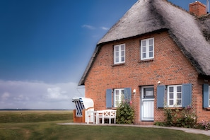 Ein Haus mit Backsteinfassade, einem Strohdach, einer weißen Tür und blauen Fensterläden.