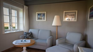Ein Zimmer mit einer Couch, einem Tisch, einer Lampe und zwei gerahmten Bildern an der Wand.