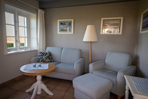 Ein Zimmer mit einer Couch, einem Tisch, einer Lampe und zwei gerahmten Bildern an der Wand.