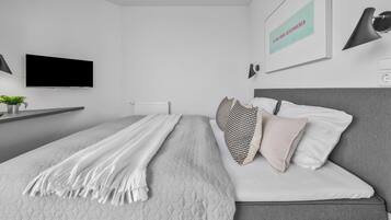 A modern bedroom with a bed, a TV, a radiator, and a wall-mounted lamp.