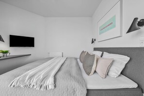 Une chambre moderne avec un lit, un téléviseur, un radiateur et une lampe fixée au mur.
