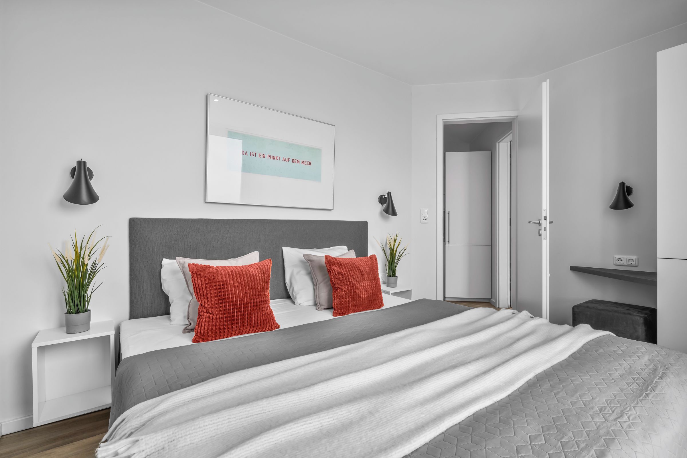 Ein modernes Schlafzimmer mit einem großen Bett, zwei Nachttischen, einer Kopfteil, einer Wandleuchte, einer Tür und einem kleinen Topfpflanzen.