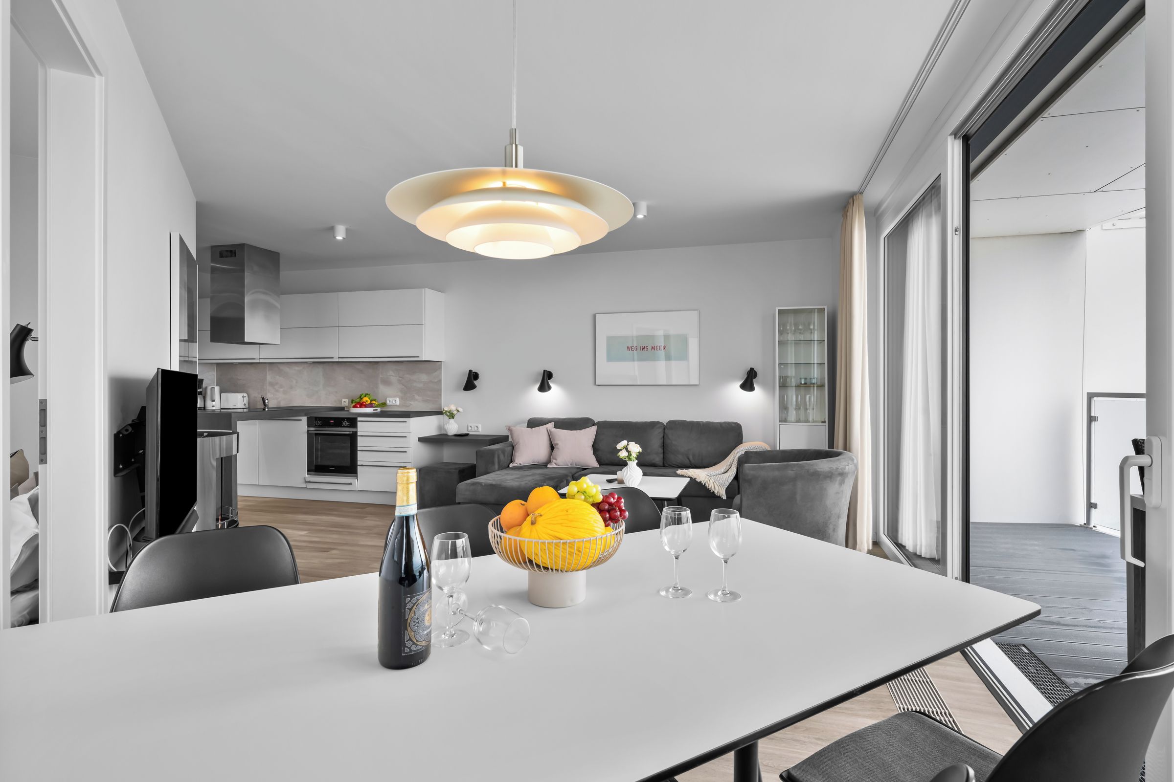 A modern dining area with a white table, a bottle of champagne, and glasses.
