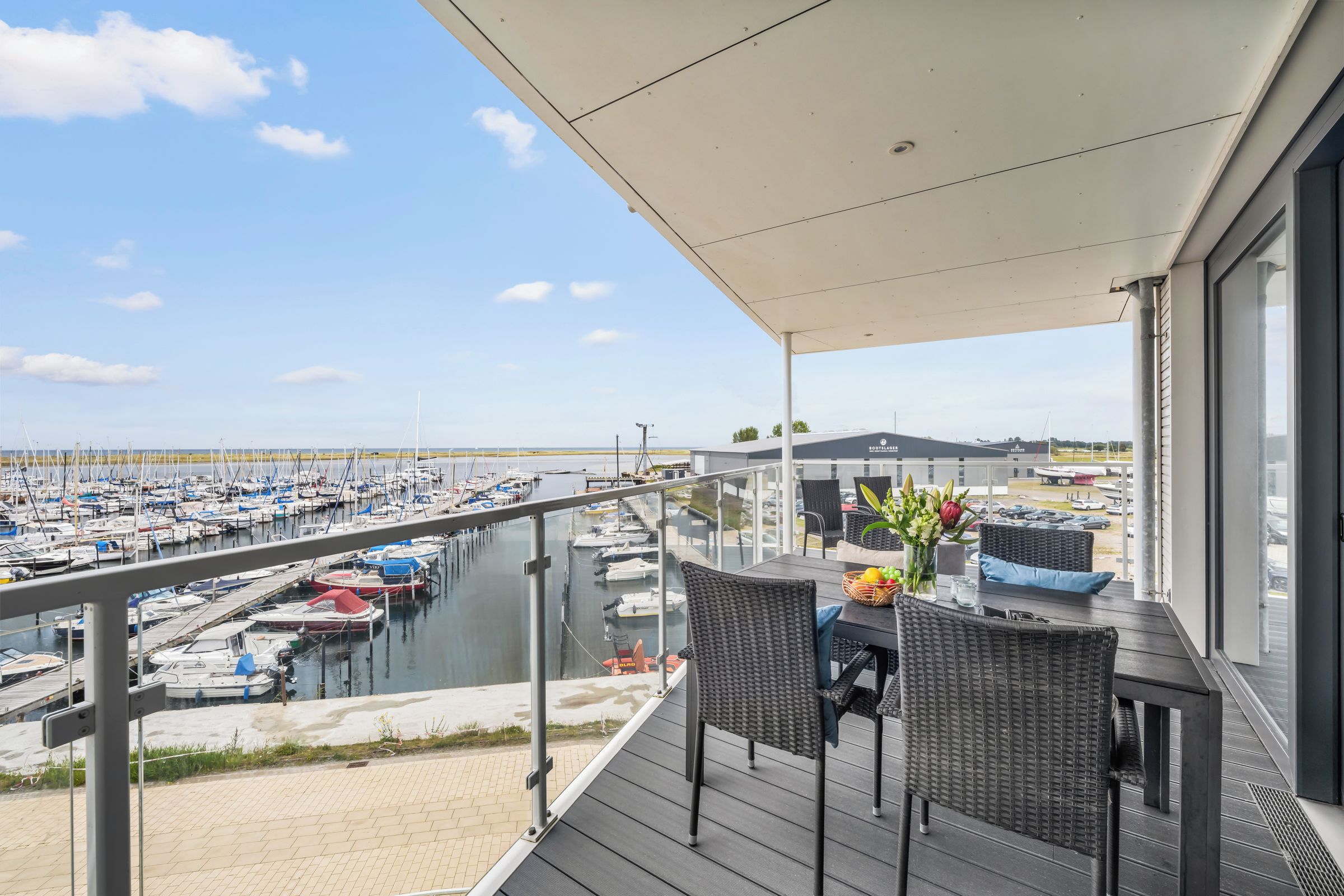 Ein Balkon mit Korbmöbeln, mit Blick auf einen Yachthafen und zahlreiche Boote.
