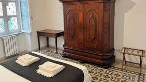 A bedroom with a bed, a wooden wardrobe, a small table, and a window with a geometric pattern. - Gianicolo Hill Apartment (Roma)