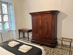 Ein Schlafzimmer mit einem Bett, einem Holzschrank, einem kleinen Tisch und einem Fenster mit geometrischem Muster.