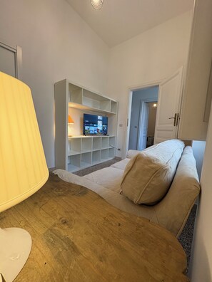 Ein Wohnzimmer mit Fernseher, einer Couch, einer Lampe und Holzboden.