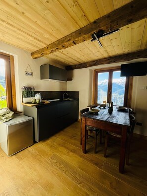 A compact kitchen with a dining area, wooden ceiling beams, and a view of mountains. - Maison Terese - A cozy retreat surrounded by nature and tranquility (Gressan)