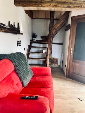 A red sofa with a remote control, a wooden staircase, and a sign on the wall. - Maison Terese - A cozy retreat surrounded by nature and tranquility (Gressan)
