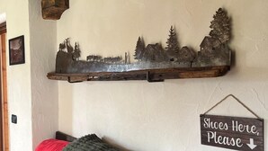 Ett vardagsrum med en röd soffa, en dekorativ metallhylla med en bild av ett lantligt motiv och en skylt som visar var man förvarar sina skor.