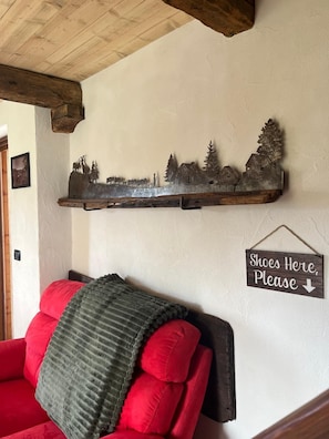 A living room with a red sofa, a decorative metal shelf with a rural scene, and a sign indicating a shoe storage area. - Maison Terese - A cozy retreat surrounded by nature and tranquility (Gressan)