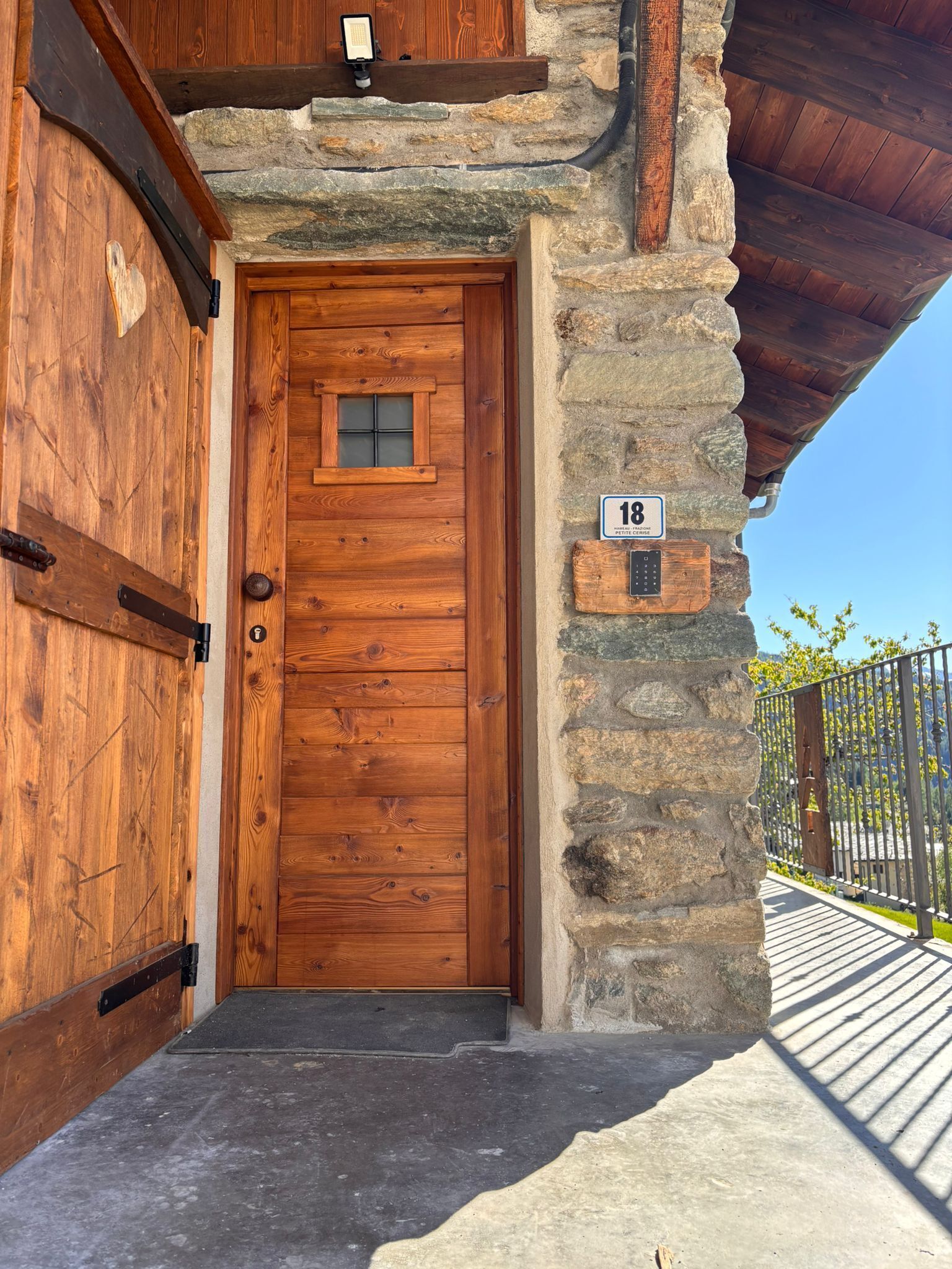 A rustic wooden door with a small window, a stone wall, and a metal gate.