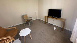 Ein Wohnzimmer mit Fernseher auf Holzständer, Schaukelstuhl, weißem Tisch und braunem Sofa.