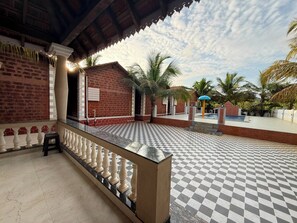 A covered outdoor area with a checkered floor, a pool, and palm trees.