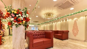 A hotel lobby with a marble floor, red leather sofas, a large floral arrangement, and a decorative ceiling light. - EENNRA ATTRAYEE GUEST HOUSE  & BANQUET (Balurghat)