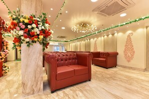 Un hall d’hôtel avec un sol en marbre, des canapés en cuir rouge, un grand arrangement floral et un lustre décoratif au plafond.