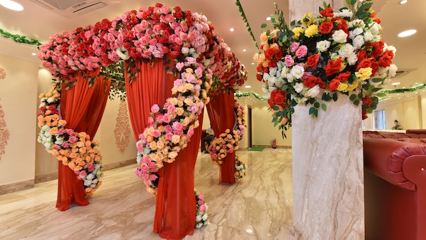 A room with a marble floor, red curtains, and floral arrangements.