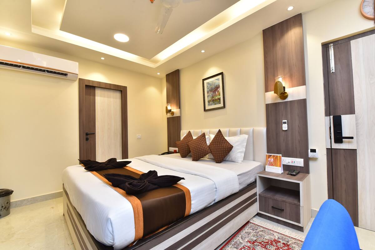 A hotel room with a bed, bedside table, nightstand, wardrobe, and an air conditioning unit.