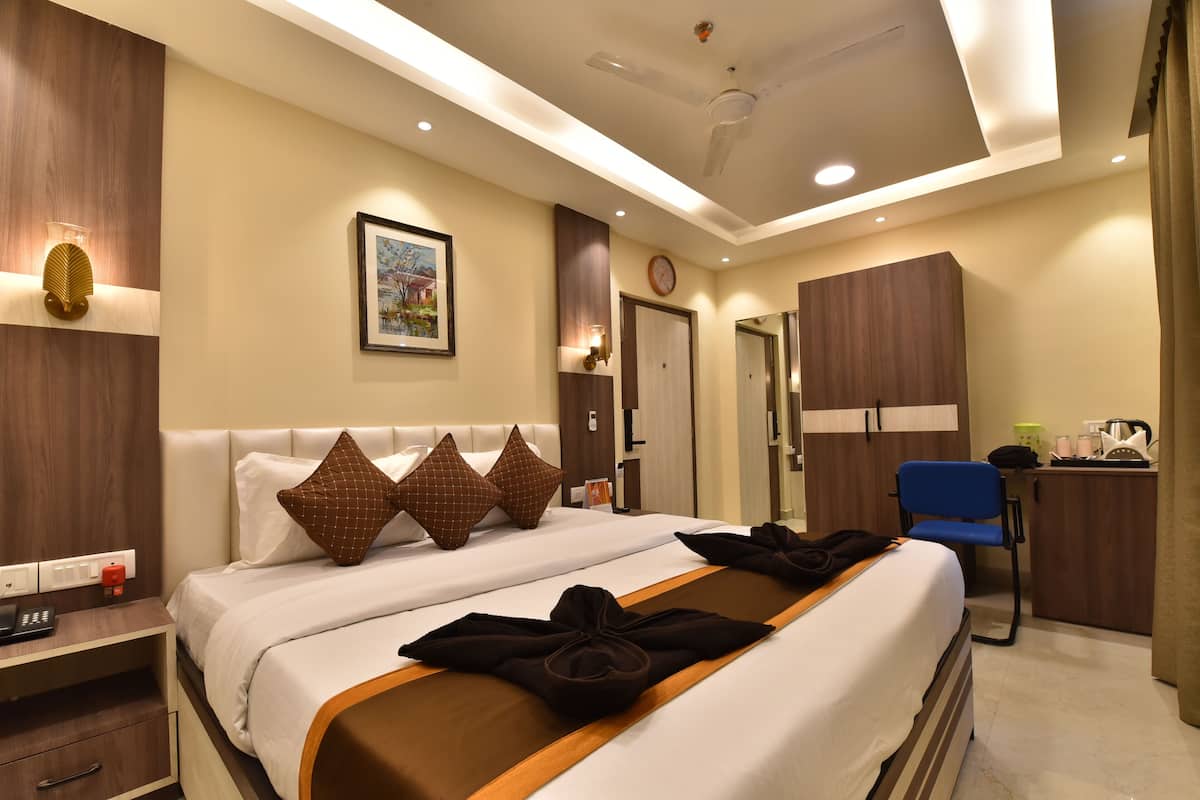 A hotel room with a large bed, bedside tables, a desk, a chair, and a wardrobe.