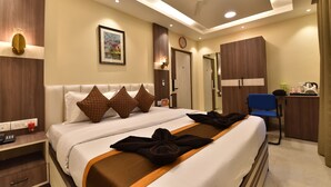 A hotel room with a large bed, bedside tables, a desk, a chair, and a wardrobe.