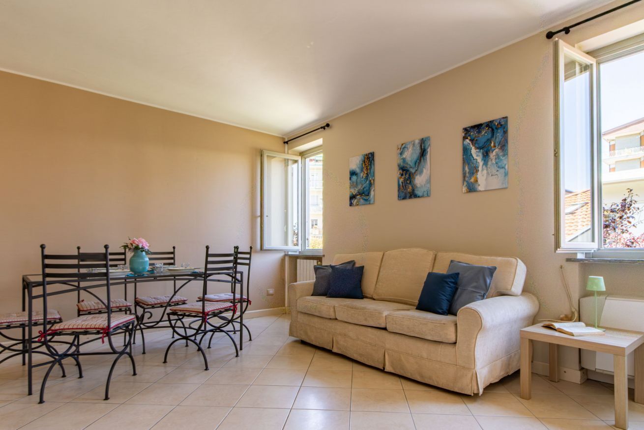 Un salon avec un canapé beige, une table à manger avec des chaises et trois tableaux abstraits accrochés au mur.