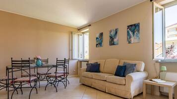 Un salon avec un canapé beige, une table à manger avec des chaises et trois tableaux abstraits accrochés au mur.