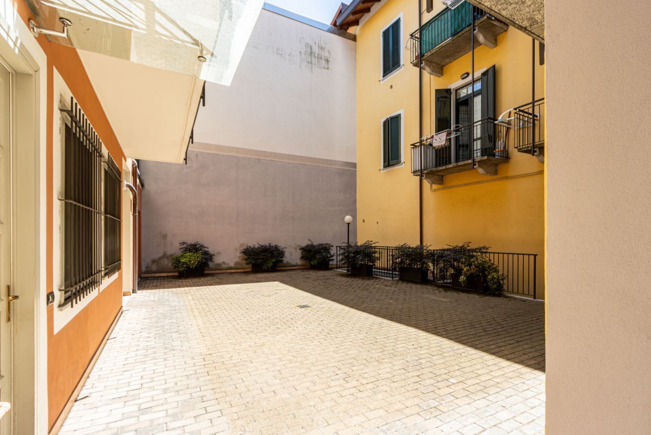 Un cortile con pavimento in pietra, un edificio con facciata gialla e un cancello in metallo.