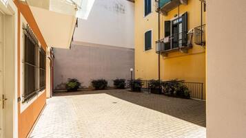 Un cortile con pavimento in pietra, un edificio con facciata gialla e un cancello in metallo.