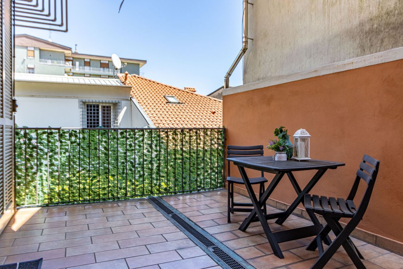 Un patio con tavolo e sedie, una recinzione verde e un edificio con tetto in tegole sullo sfondo.